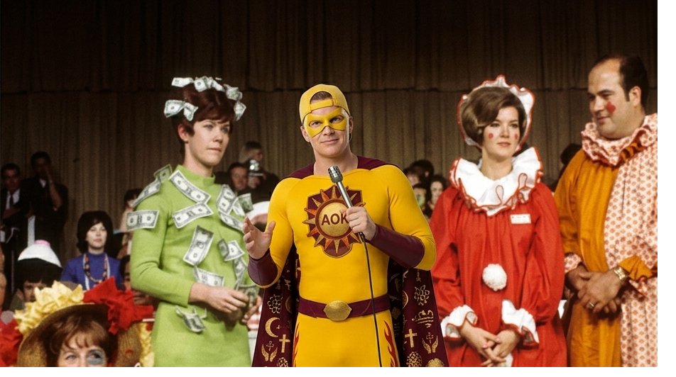 AOK Man stands on a game-show stage between Door 1 and Door 3, hands on hips, fully owning the bit — confetti falls, costumed contestants cheer in the background